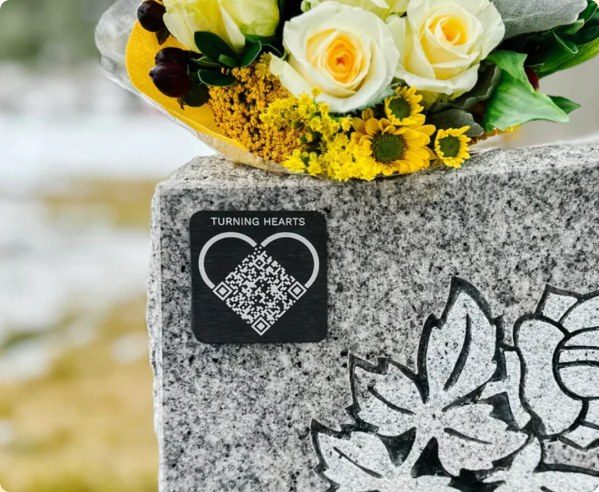 A Turning Hearts medallion on a granite headstone beside fresh flowers