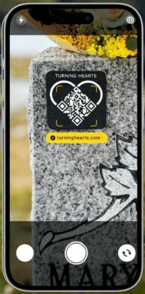 A phone scanning a real Turning Hearts medallion on a granite headstone